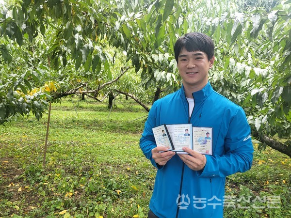 이국진 대표가 복숭아 농장에서 그동안 취득한 각종 농업 자격증들을 들고 환하게 웃고 있다.