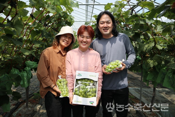 신젠타 청년농업인 네트워크 프로그램 2기에 선정된 박상윤 대표(가운데)가 가족이자 동업자인 오빠, 어머니와 함께 샤인머스캣을 들고 환하게 웃고 있다.