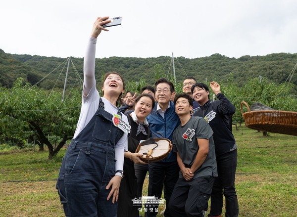 이재명 대통령(가운데)이 간담회에 앞서 청년농업인들과 복숭아 과원에서 셀카를 찍고 있다. [대통령실 제공]