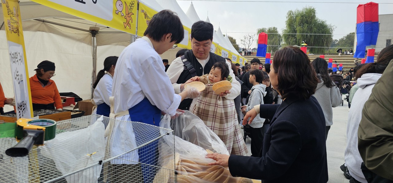 아빠 품에 안긴 아기가 갓 만든 뻥튀기에 손을 내밀고 있다.