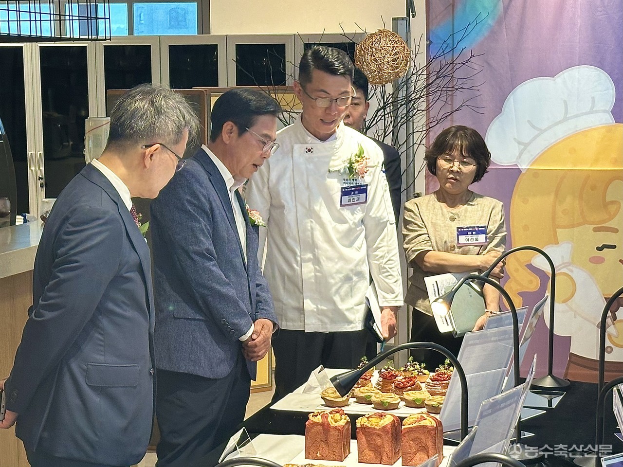이인재 (사)대한제과협회 천안시지장이 김석필 천안시부시장, 이경직 백석문화대학총장에게 출품한 작품의 개발 의도와 농특산물 활용 방안 등을 설명하고 있는 모습.(왼쪽부터)&nbsp;이경직 백석문화대학총장,&nbsp;김석필 천안시부시장,&nbsp;이인재 (사)대한제과협회 천안시지장, 이선희 식품안전과장